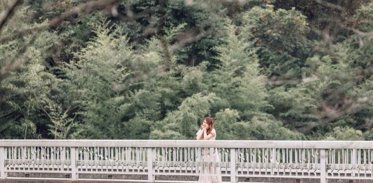 A woman stands on a bridge surrounded by lush greenery, embodying a serene summer vibe.