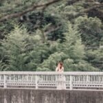 A woman stands on a bridge surrounded by lush greenery, embodying a serene summer vibe.