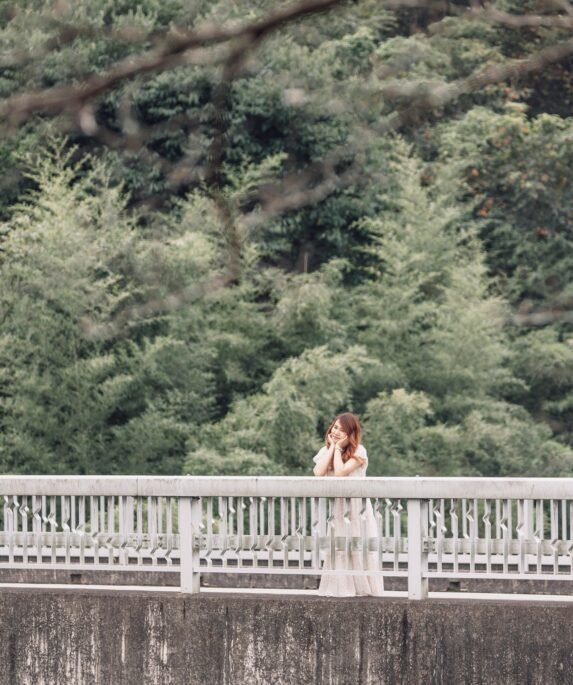 A woman stands on a bridge surrounded by lush greenery, embodying a serene summer vibe.
