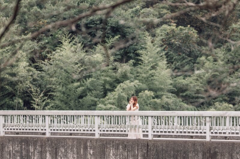 A woman stands on a bridge surrounded by lush greenery, embodying a serene summer vibe.