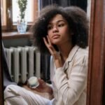 A woman applies skincare cream in a cozy home environment during her morning routine.