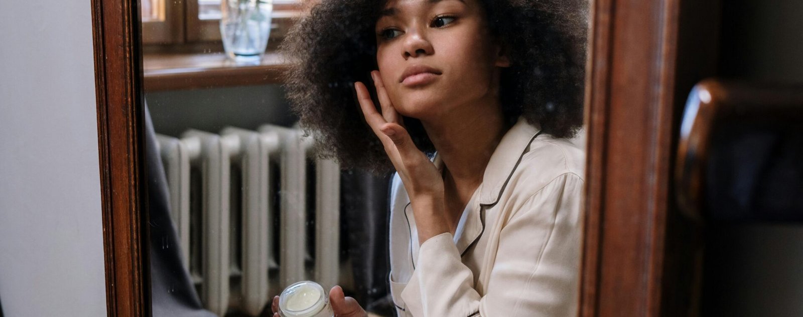 A woman applies skincare cream in a cozy home environment during her morning routine.