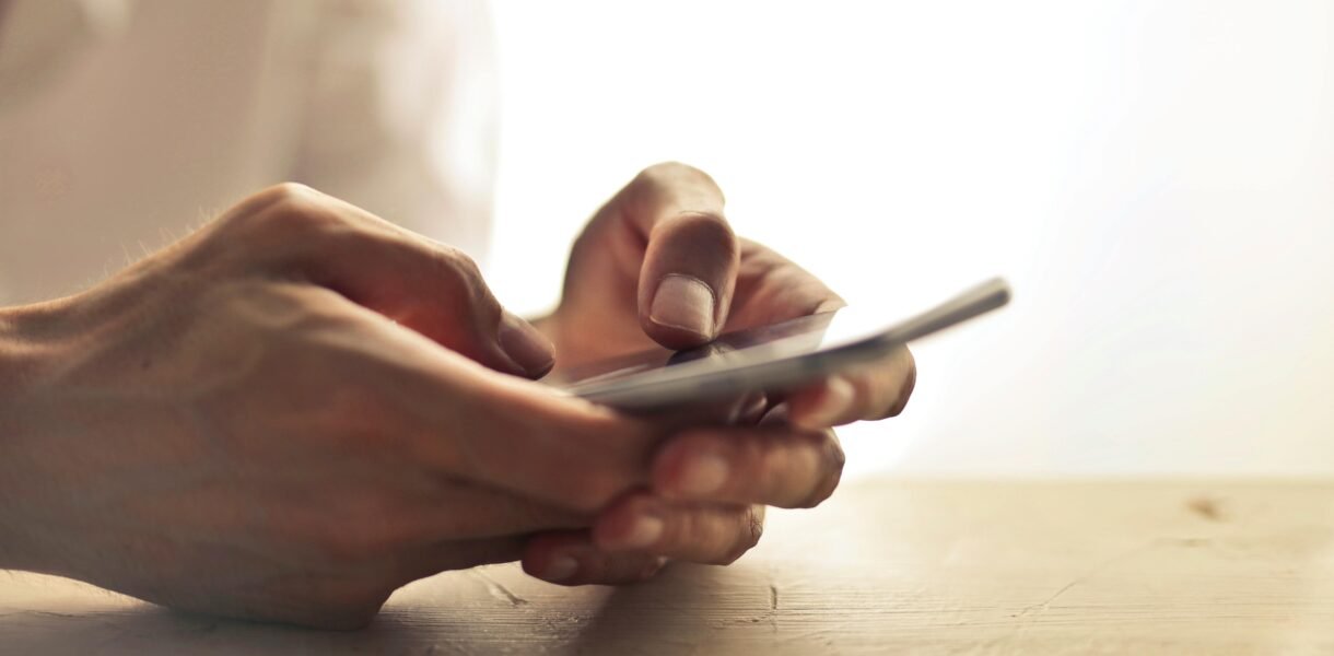 Close-up of an individual's hands holding a smartphone on a table indoors.