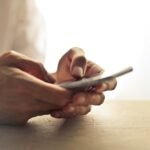Close-up of an individual's hands holding a smartphone on a table indoors.