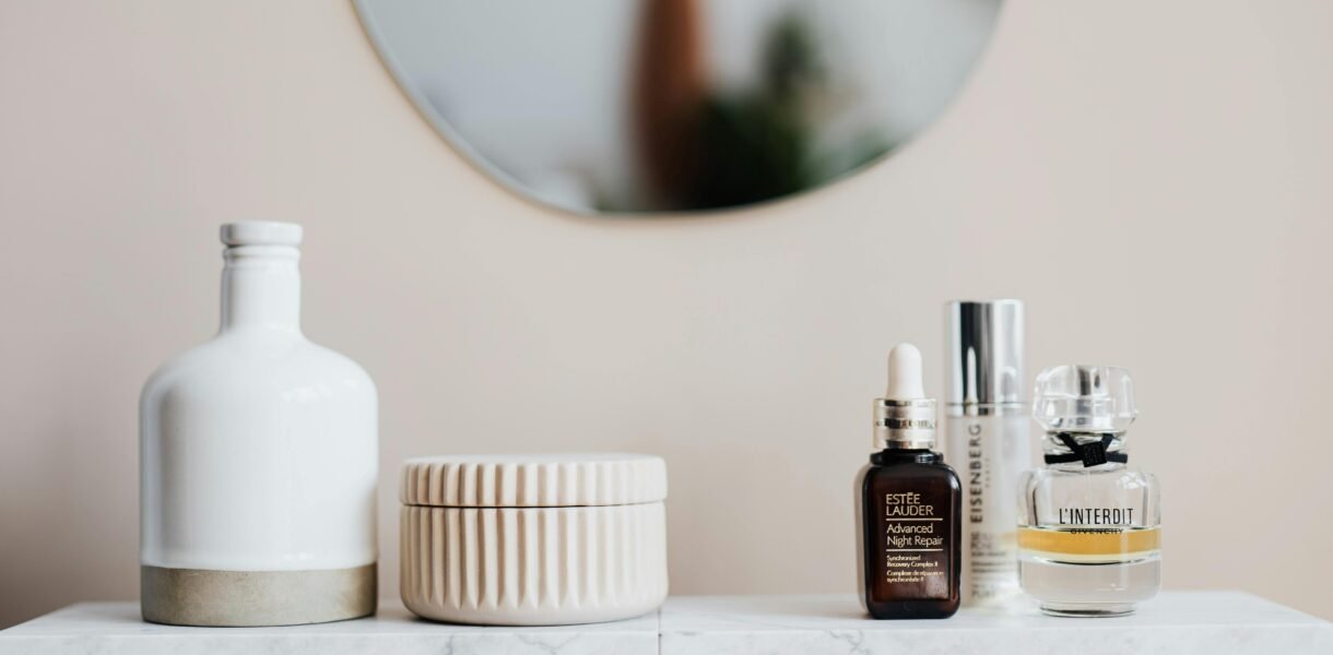 Stylized skincare and cosmetic bottles on a marble shelf with mirror reflection.