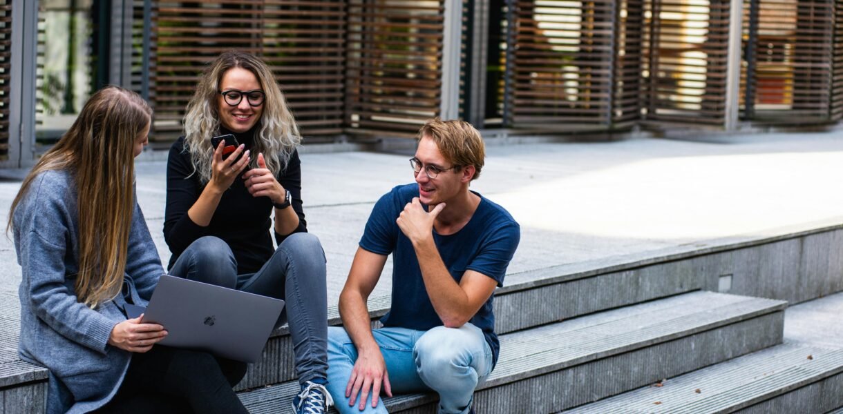 Three young professionals having a friendly chat while sitting on outdoor steps.