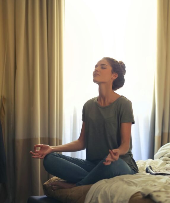 Adult woman practicing meditation on her bed surrounded by a calm bedroom atmosphere.