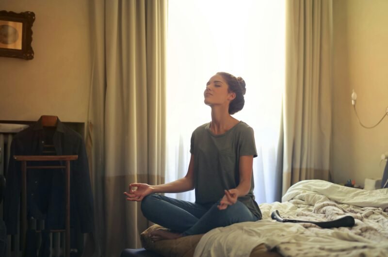 Adult woman practicing meditation on her bed surrounded by a calm bedroom atmosphere.